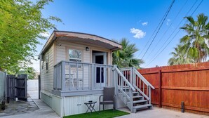 A small, single-story house with a front porch, a staircase leading to the entrance, and a fenced backyard. - Private Tiny House Retreat with Spacious Patio, Free Parking & WiFi (Las Vegas)