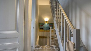 Una escalera con barandilla de madera y pared blanca. Se ve un cartel con texto al fondo.