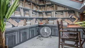 Un rincón acogedor para leer con una estantería llena de libros, un ventilador y un sillón.