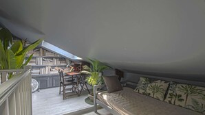 Un dormitorio de altillo acogedor con techo inclinado, un escritorio pequeño con silla, una cama con cojín estampado y una planta en maceta.