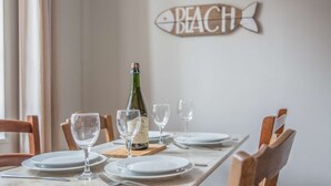 Una mesa de comedor dispuesta con platos, vasos y una botella de vino, con un cartel que dice 'BEACH' en la pared.