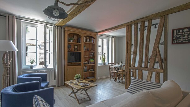 Un salón acogedor con una estantería de madera, un comedor con mesa y sillas, y un amplio ventanal que proporciona luz natural.