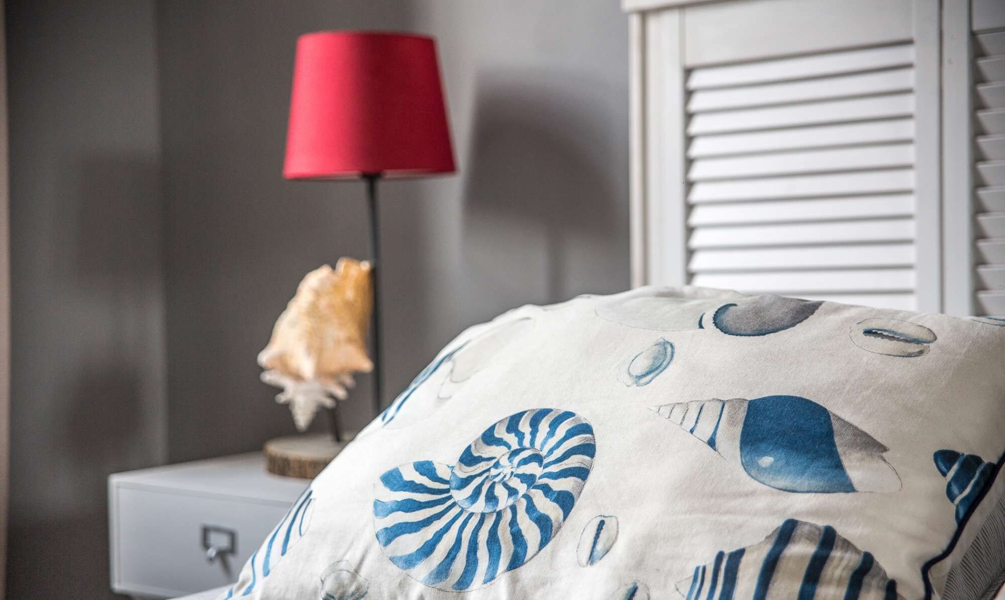 A bedroom with a bed, a nightstand, a lamp, and a decorative shell pillow.