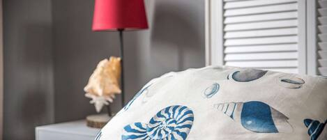 A bedroom with a bed, a nightstand, a lamp, and a decorative shell pillow.