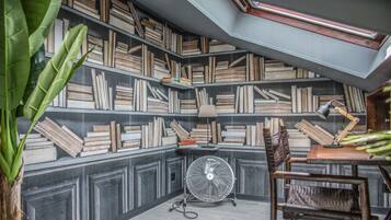 A cozy reading nook with a bookshelf filled with books, a fan, and a chair.