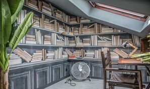 Un rincón acogedor para leer con una estantería llena de libros, un ventilador y un sillón.