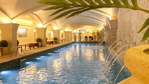 Una piscina interior de forma alargada, rodeada de zonas de estar y plantas en macetas.