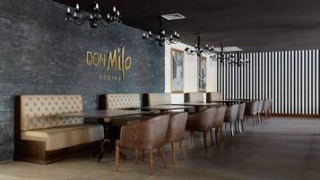 A modern restaurant interior with a long dining table, cushioned benches, and a dark brick wall with the name 'DON MILO CU CINA'.
