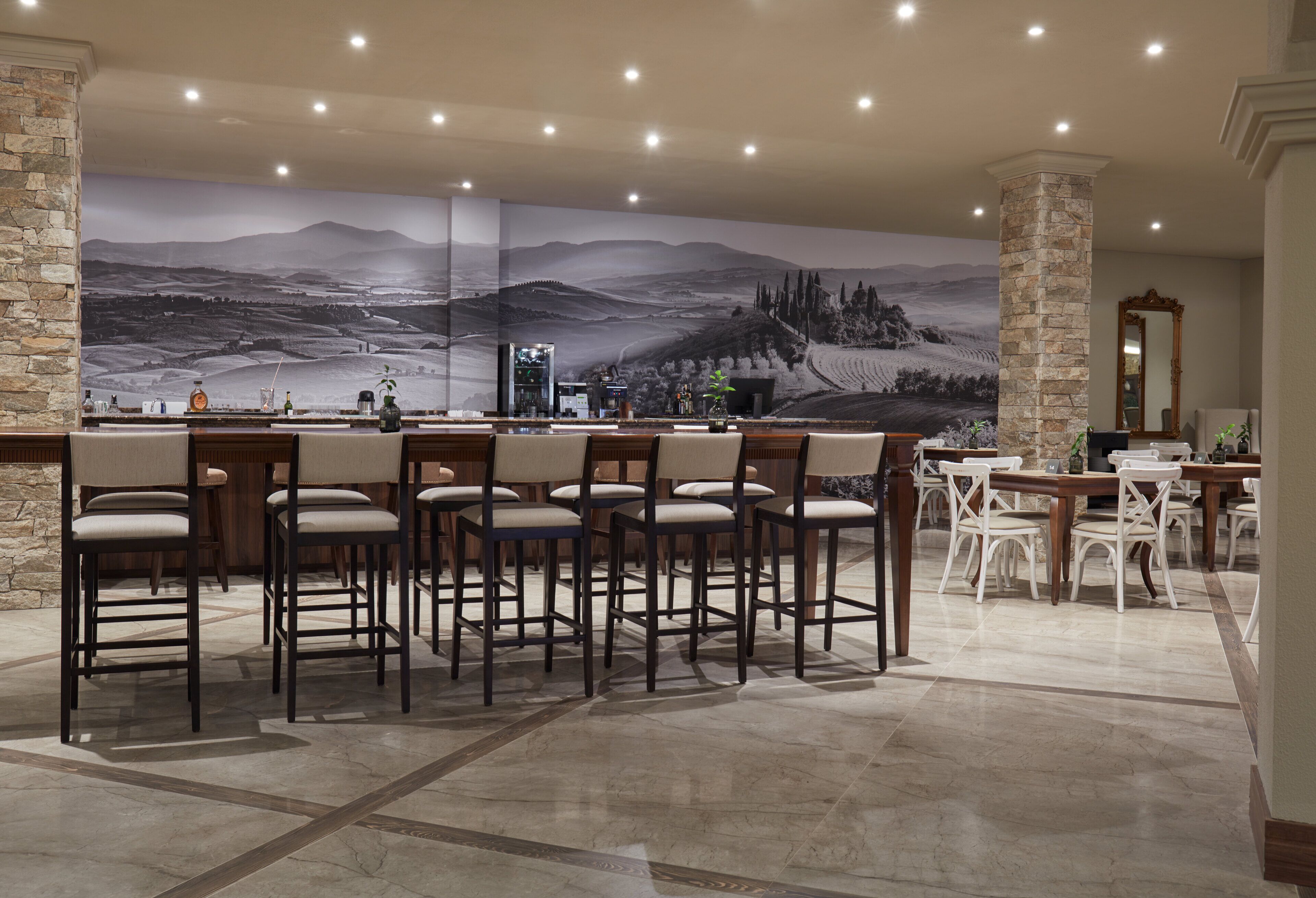 A bar area with multiple stools and a large mural of a landscape.