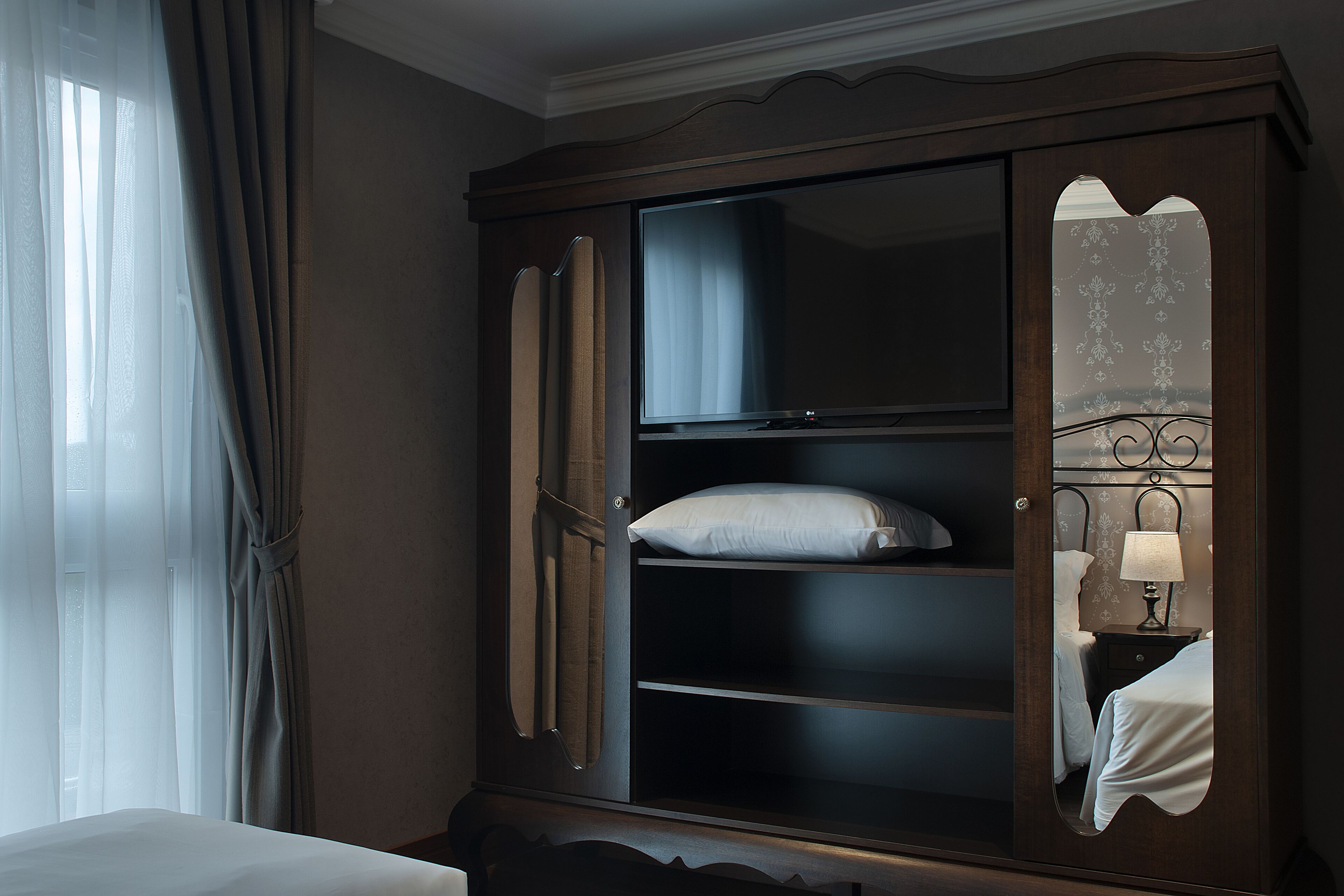 A hotel room with a large wardrobe, a bed, and a nightstand with a lamp.