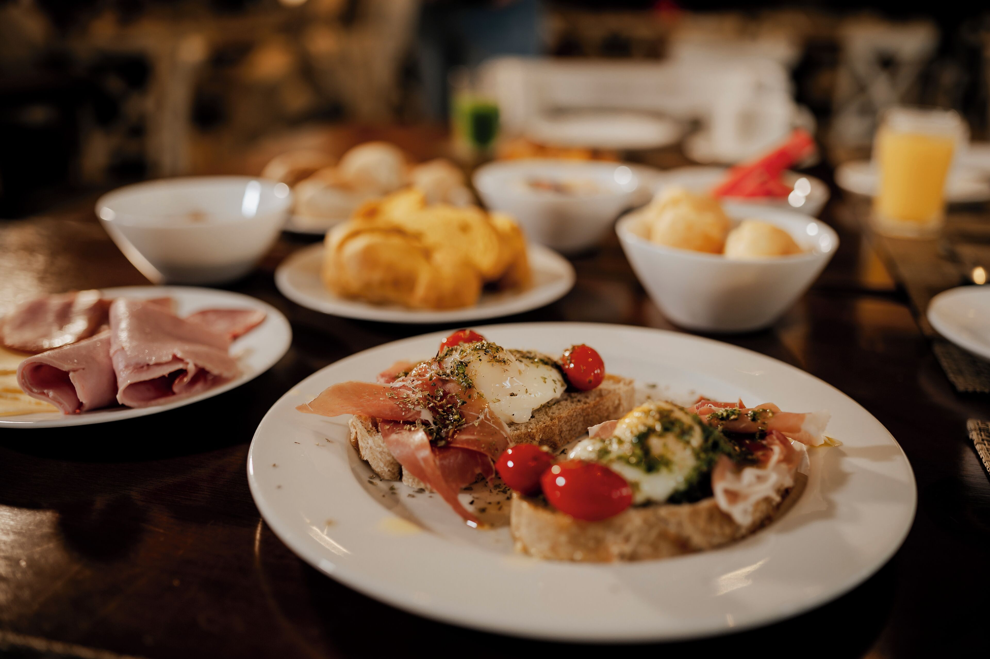 A dining table with various dishes including bread with toppings, a bowl of soup, and a plate of sliced meat.