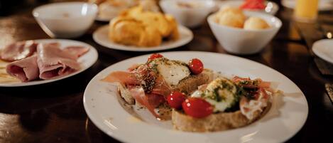 A dining table with various dishes including bread with toppings, a bowl of soup, and a plate of sliced meat.