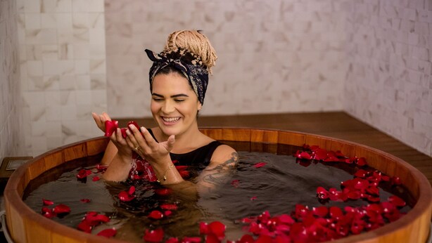 Una mujer en una bañera de madera llena de agua y pétalos de rosa.
