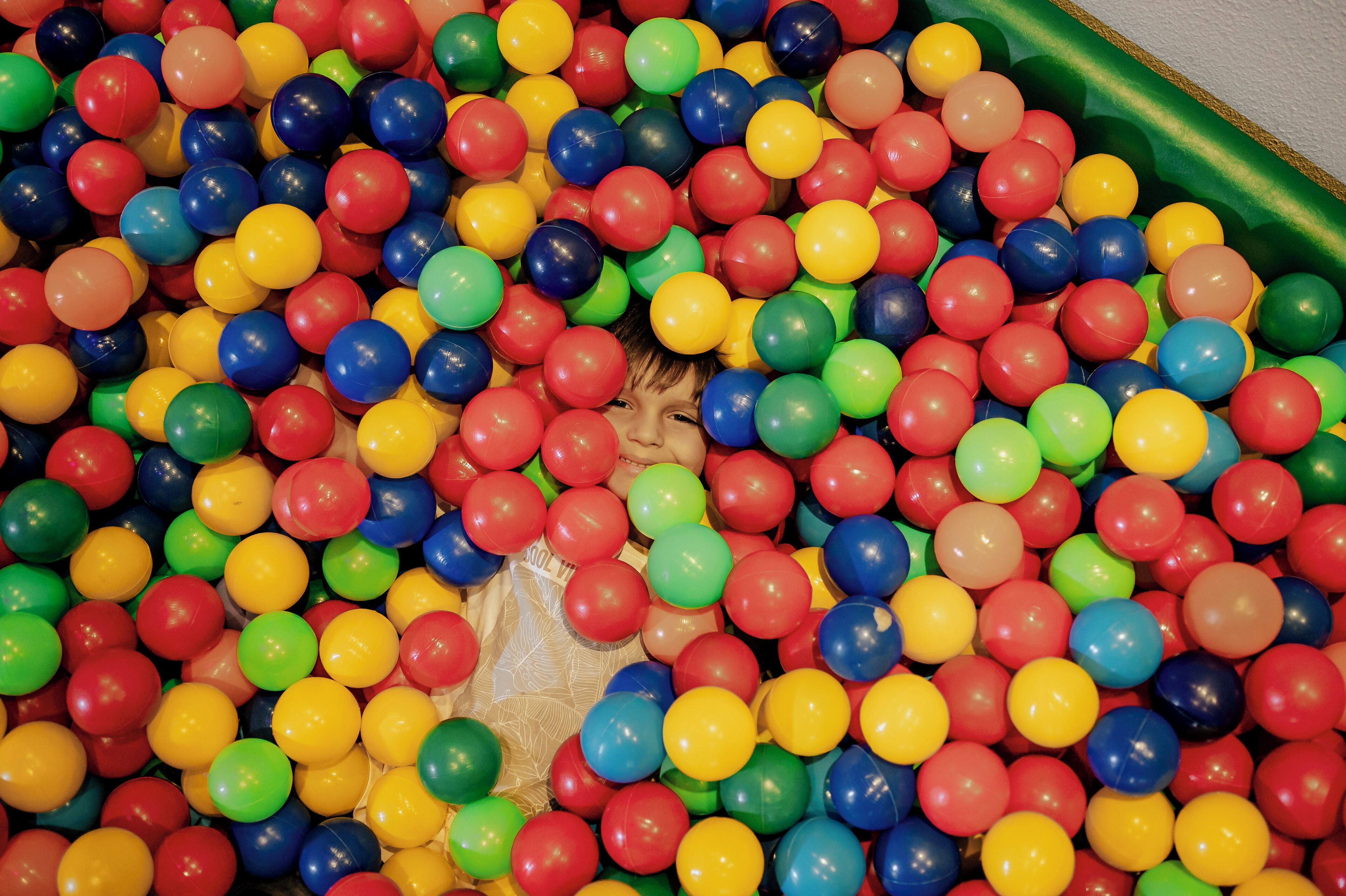 Un niño rodeado por un pozo de pelotas lleno de bolas de plástico multicolores.