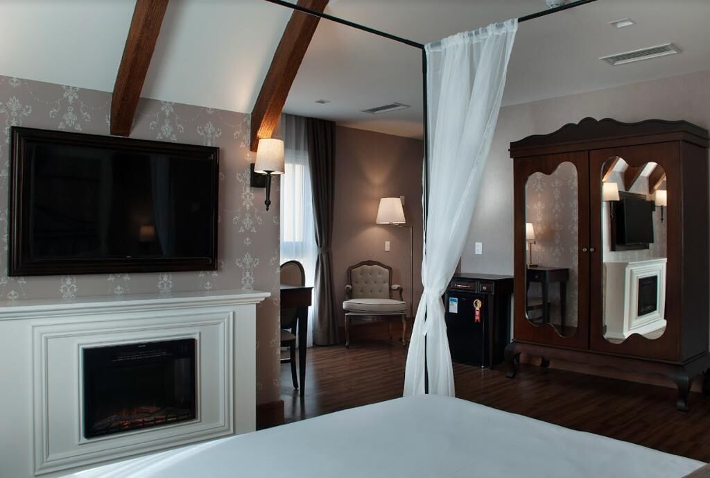 Una habitación de hotel con chimenea, un televisor montado en la pared, un mueble de madera grande y una silla.