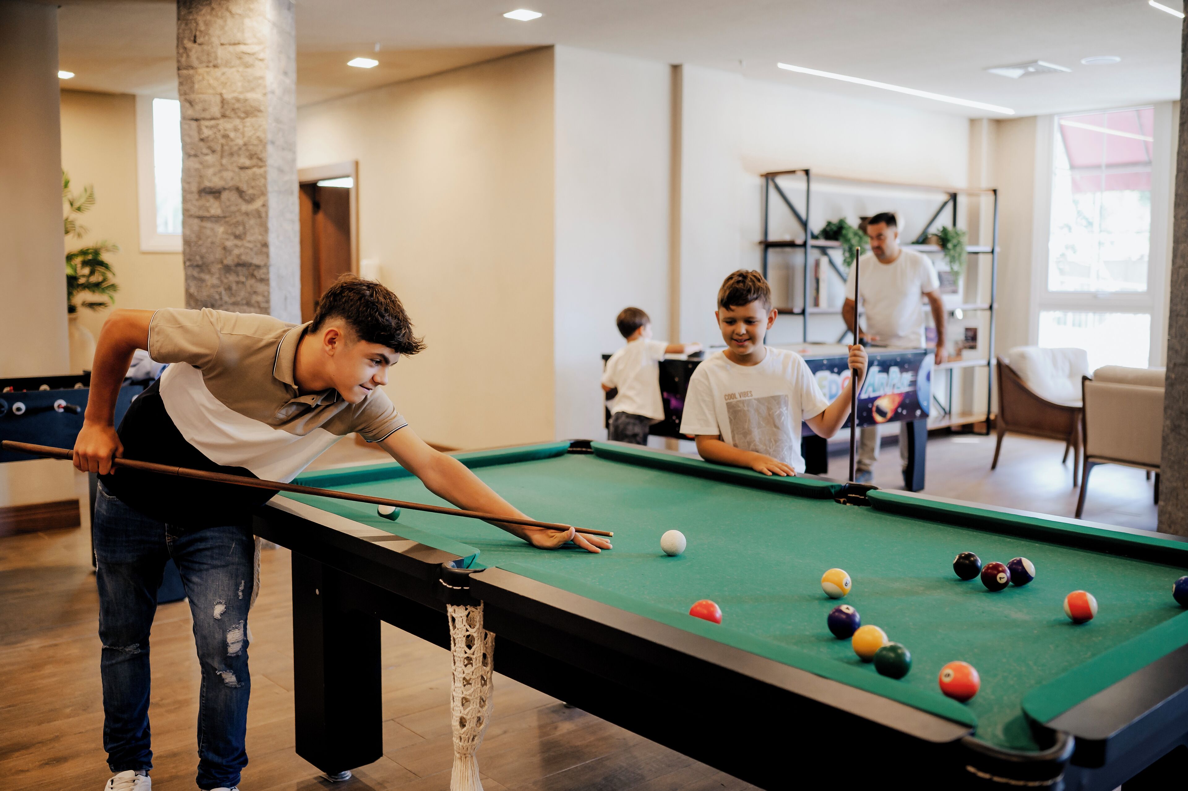 A pool table in a room with a modern interior, including a stone pillar and a bookshelf.