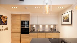 A modern kitchen with wooden cabinets, a built-in oven, a coffee machine, and a large island. - Edinburgh Luxury Apartment- The Matisse Suite (Edinburgh)