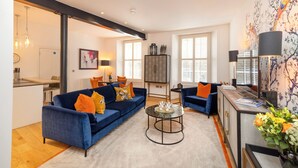 A modern living room with a blue sofa, a coffee table, and a kitchen area visible in the background. - Edinburgh Luxury Apartment- The Matisse Suite (Edinburgh)