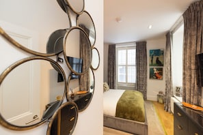 A bedroom with a bed, a dresser, a mirror, and a window with curtains. - Edinburgh Luxury Apartment- The Matisse Suite (Edinburgh)