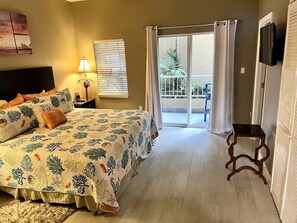A bedroom with a bed, a nightstand, a lamp, a TV, and a balcony with curtains. - Blue Chair Dream 1-102 (Cruz Bay)