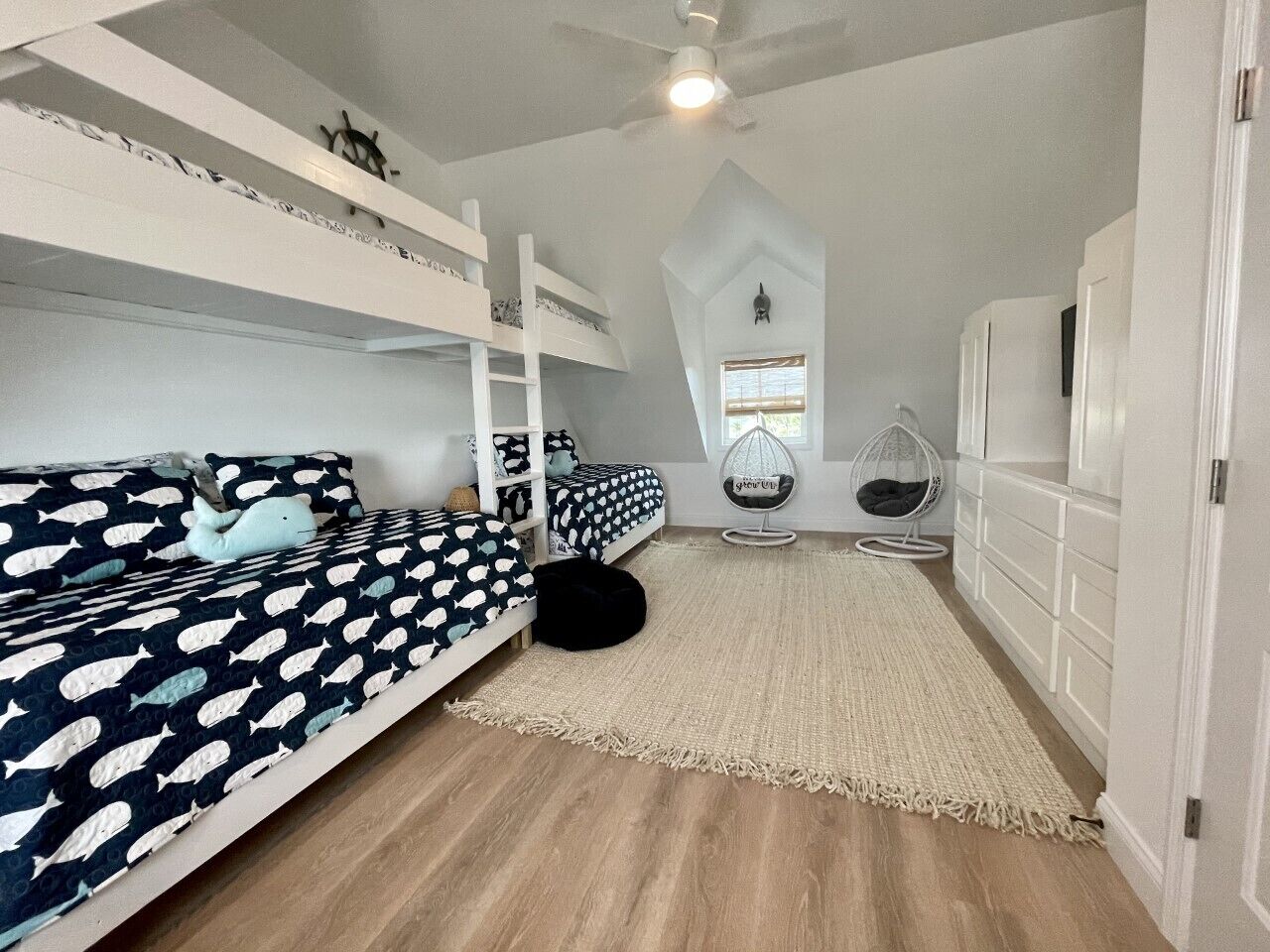 Quarto com beliches, uma cadeira suspensa e uma janela grande.