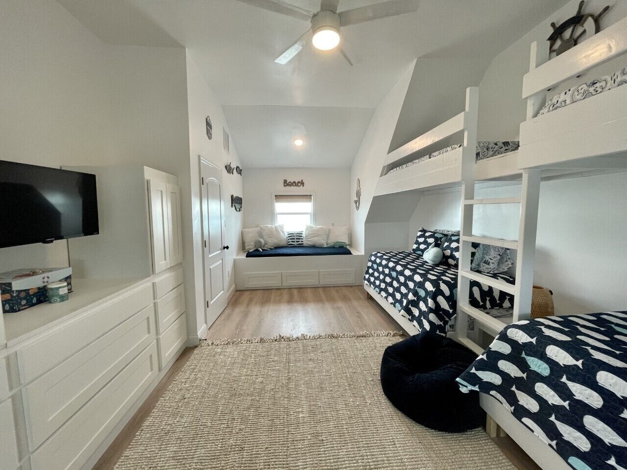 A bedroom with bunk beds, a television, a window, and a ceiling fan.