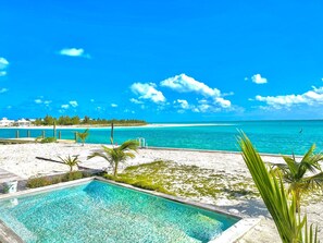 A pool with clear blue water, surrounded by a sandy beach and palm trees, overlooking a turquoise sea and a distant island. - luxurious home with 360 degree ocean views (Treasure Cay)