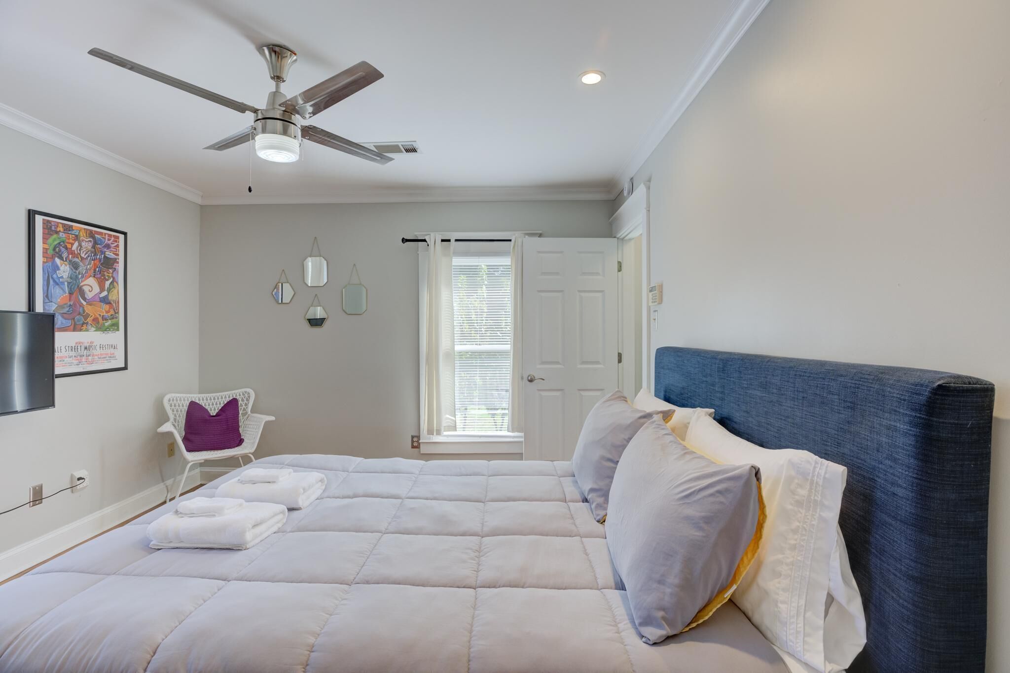 Un dormitorio con cama, ventilador de techo, ventana con persianas, una silla y una puerta.