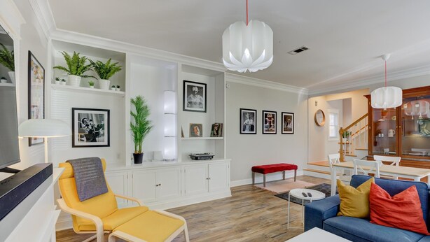 Een moderne woonkamer met een bank, een gele fauteuil en een eethoek met een tafel en stoelen.