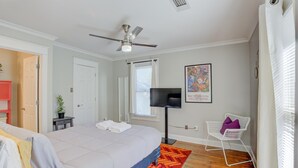 Een slaapkamer met een bed, een plafondventilator, een televisie, een stoel en een raam.