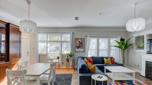 Een woonkamer met een blauwe bank, een witte salontafel en een kleurrijk gestreept vloerkleed.