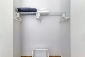 A small, white closet with a metal shelf and a plastic laundry basket.