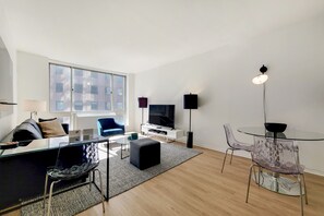 A modern living room with a glass coffee table, a sofa, a TV, and a dining area with a glass table and chairs.