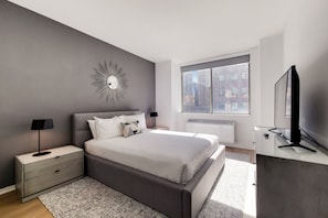 Une chambre moderne avec un grand lit, des tables de chevet, une télévision et une fenêtre donnant sur la ville.