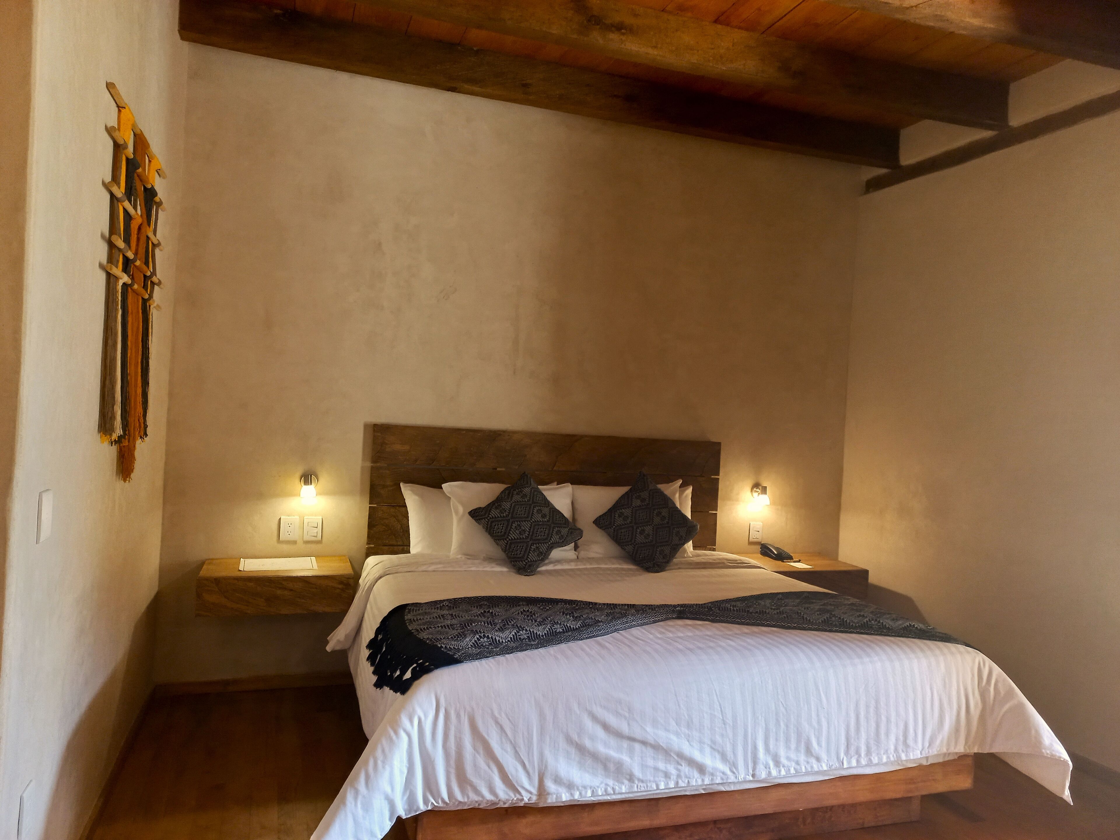 Una cama bien hecha con sábanas blancas y almohadas estampadas, un cabecero de madera y lámparas de noche.