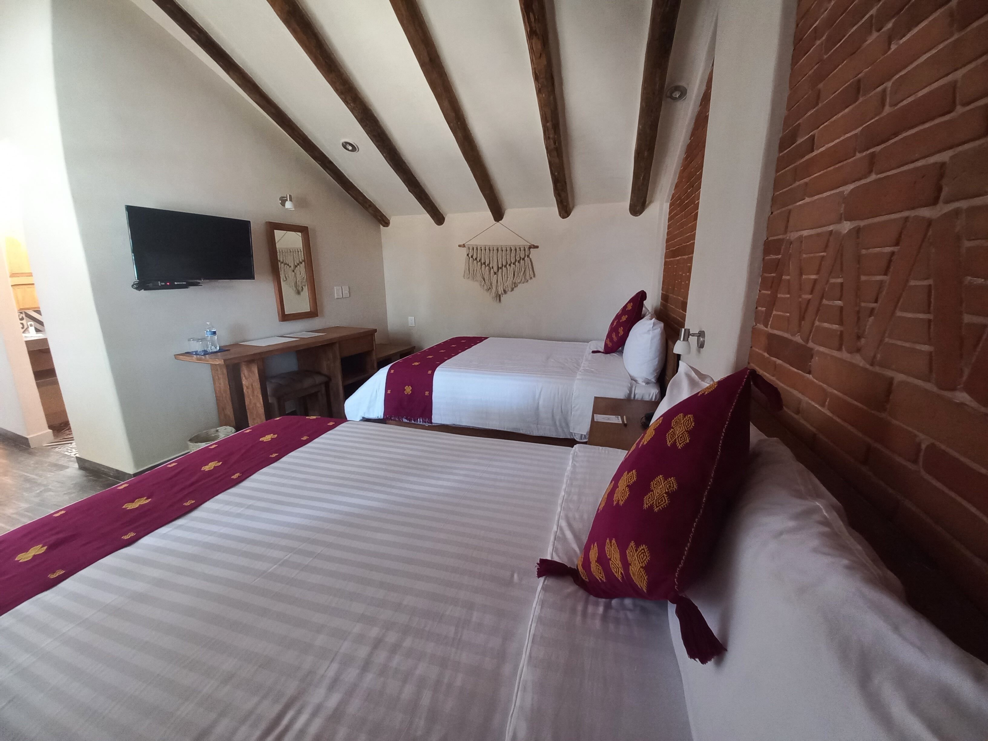 Habitación de hotel con dos camas, un escritorio, un televisor y una pared de ladrillo.