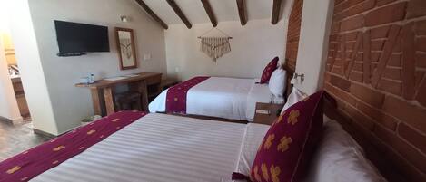 Habitación de hotel con dos camas, un escritorio, un televisor y una pared de ladrillo.