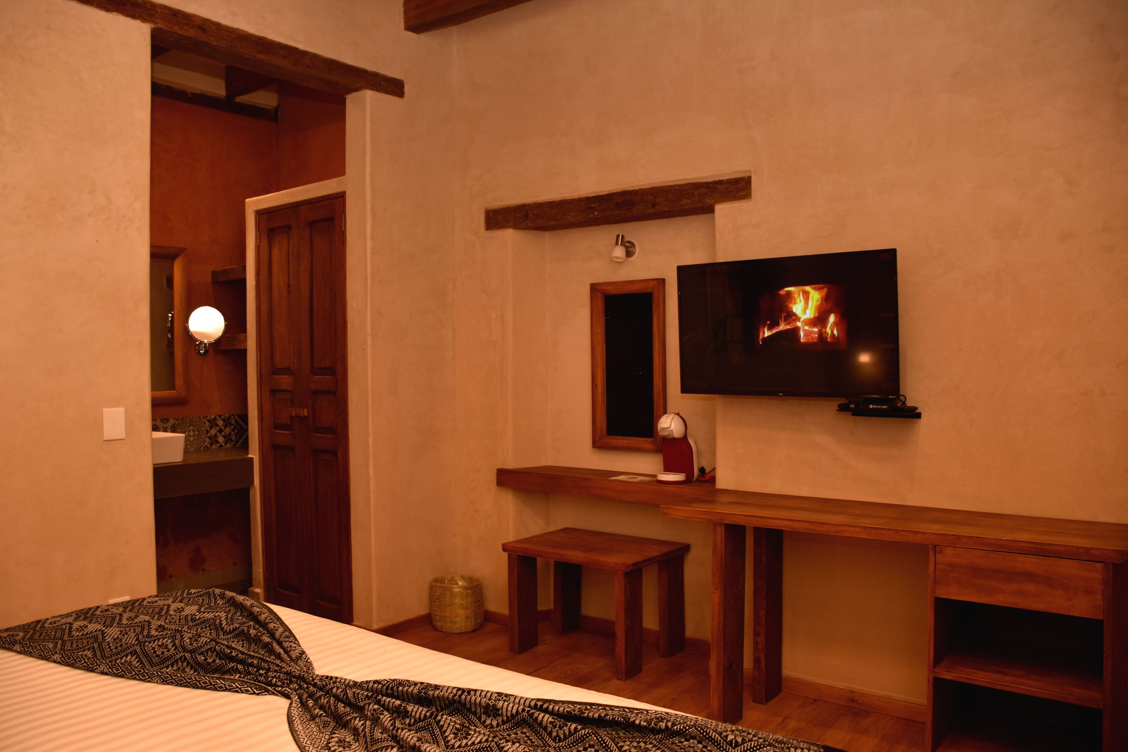 A hotel room with a bed, a wooden bench, a television mounted on the wall, and a small table.