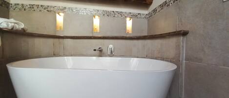 A large freestanding bathtub in a bathroom with a wooden ceiling and mosaic tile walls.