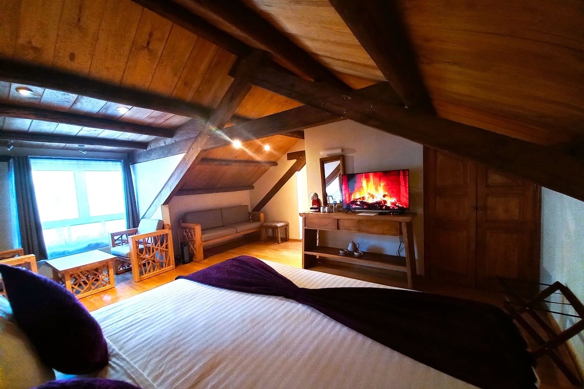 Un dormitorio acogedor en el ático, con cama, vigas de madera, chimenea y televisión.