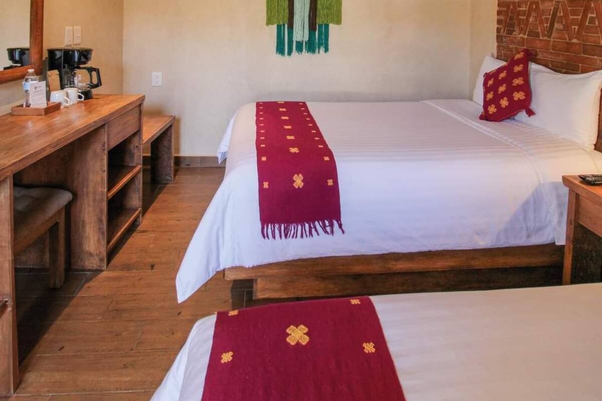 Una habitación de hotel con un escritorio de madera, una cama con una colcha roja y una pared de ladrillo.