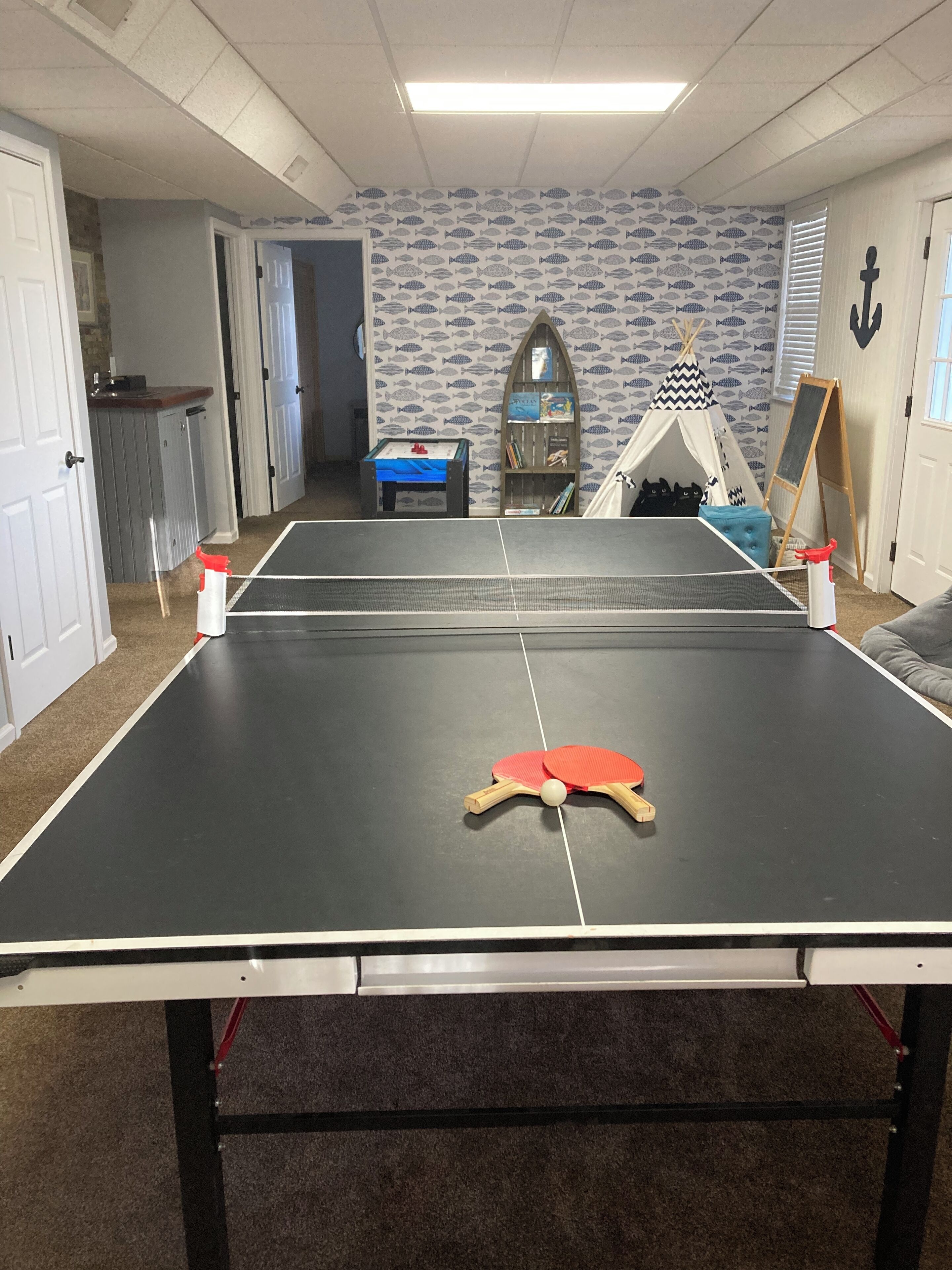 Une table de ping-pong dans une pièce dont un mur est décoré d’un motif de poissons, avec une petite bibliothèque et un tipi.