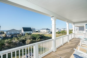 A wooden deck with white railings overlooking a beach and houses.