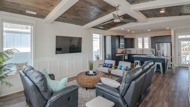 A modern living room with leather sofas, a coffee table, and a kitchen area with dark cabinets and a large island.