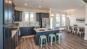 A modern kitchen with dark cabinets, a central island with stools, and a dining area with white chairs.