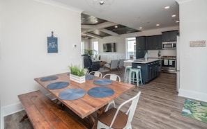 A modern kitchen with dark cabinets, a central island, and a dining area with a wooden table and chairs.