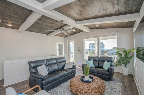 A modern living room with black leather sofas, a round woven coffee table, and a ceiling fan.