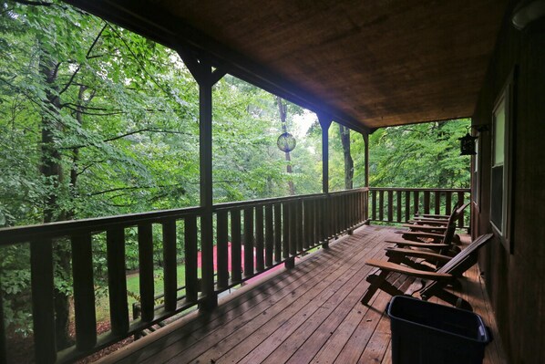 Eine Holzdielen-Terrasse mit Geländer, mit Blick auf ein bewaldetes Gebiet.