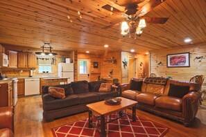 A cozy cabin interior with a wooden ceiling, a dining area with a table and chairs, a kitchen with a refrigerator and cabinets, and a living room with a sofa and a coffee table. - Carriage House Cabin #2 - Near Three Rivers (Walhonding)