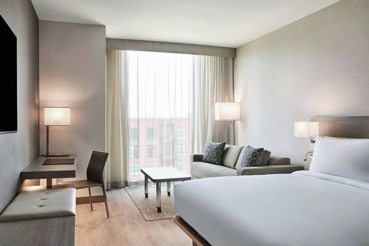 A hotel room with a large bed, a sofa, a desk, and two lamps.
